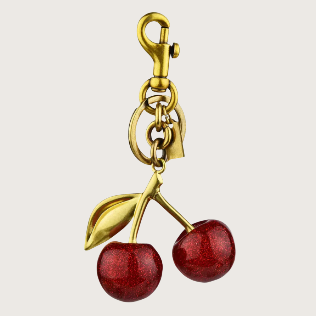 Gold cherry Bag charm with red stones on a beige background